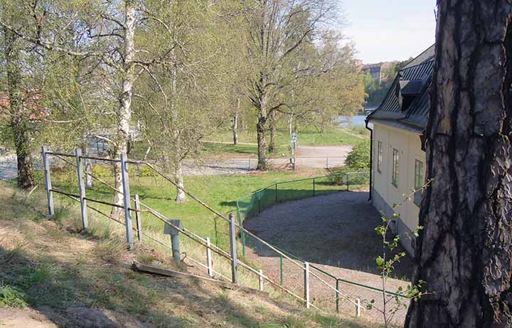 Bilden är tagen på kullen. Till höger syns det gamla kanalkontoret. Ett skyddsräcke omgärdar den nu igenfyllda ingången som ligger i slänten och vätter mot byggnaden. Foto: Henrik Lindkvist (2016).